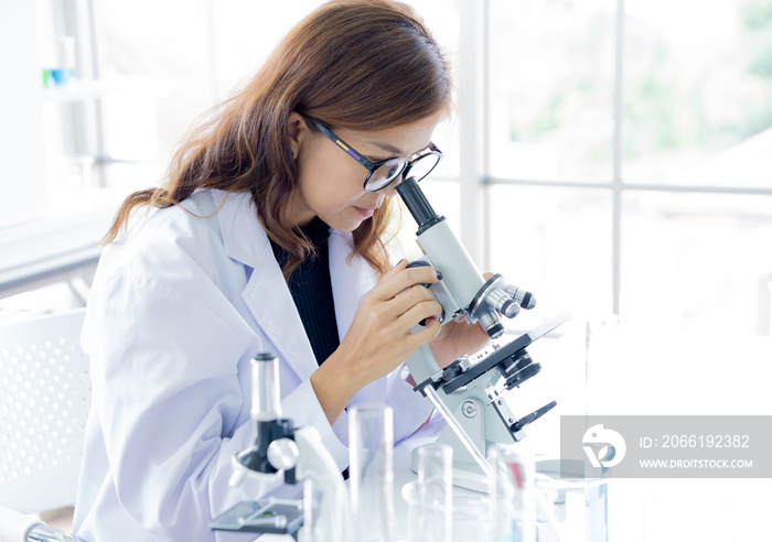 Female scientist in white coat doing a research using microscope in laboratory. Long hair asian woma