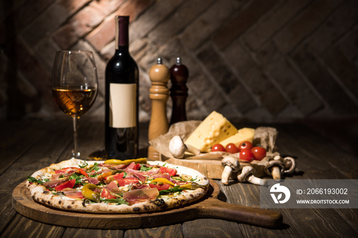 selective focus of italian pizza, spices, cheese, cherry tomatoes and bottle of wine on wooden surfa