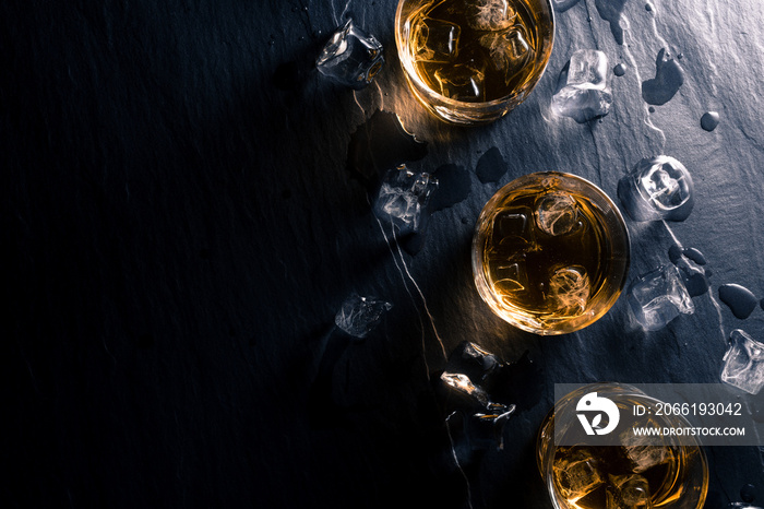 Glasses of whiskey with ice cubes on dark table