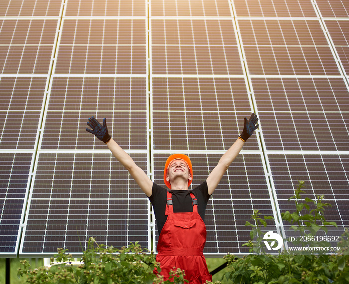 Happy successful worker near solar station raising his hands on a background of photovoltaic panels 