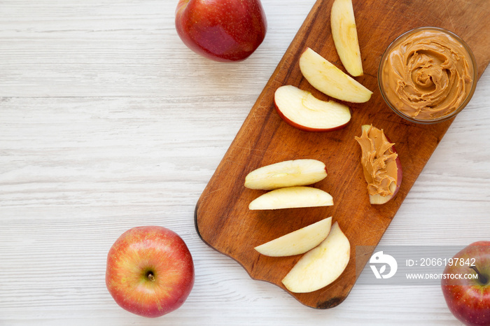 Raw Red Apples and Peanut Butter on a rustic wooden board on a white wooden table, top view. Space f