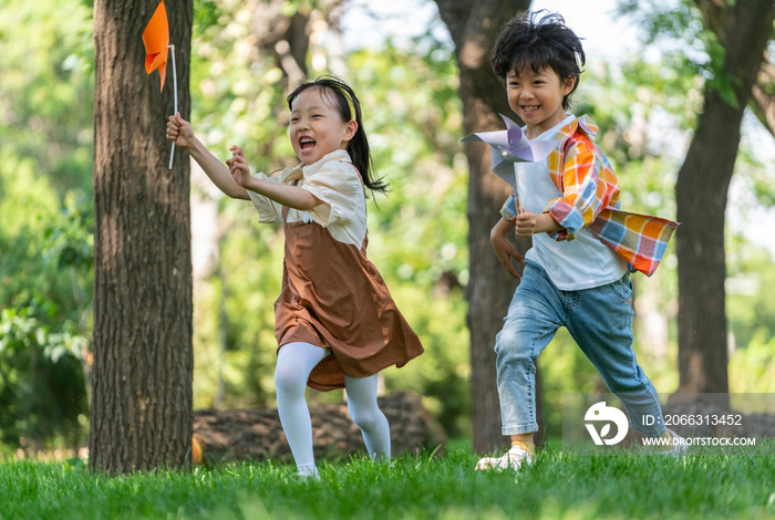 两个小孩子在草地上举着风车开心奔跑