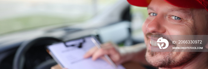 Portrait of smiling male courier driver in car salon with documents