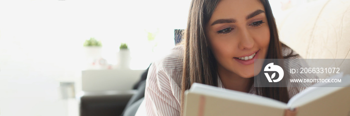 Young attractive woman reading book laying on couch at home, interesting story