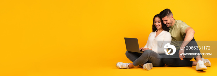 Cheerful millennial arab couple in casual sit on floor, typing in computer, surfing, work and study