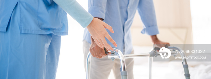 Portrait of Asian young nurse helping old elderly disable man grandfather to walk by using walker equipment in the bedroom. Senior patient of nursing home moving with walking frame and nurse support