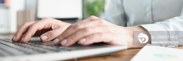 Female hands typing on laptop keyboard in office closeup