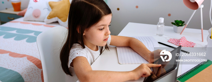 Little girl studying at home with tablet and mask on table