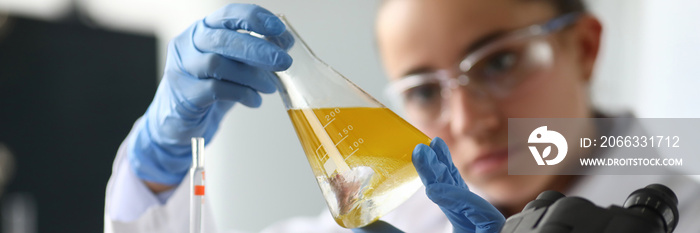 Close-up of lab assistant hands holding beaker with oil liquor. Test tube with yellow liquid. Investigation, biotechnology and pharmacy industry concept