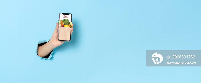 Woman hand showing smartphone using food delivery online mobile application order on internet over blue banner background. Panoramic image