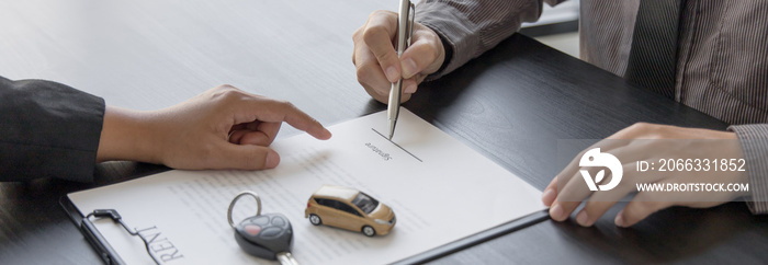 Female attendant handed over the rental car key to the customer who signed the contract and the terms of the agreement on the document, Car rental service concept.