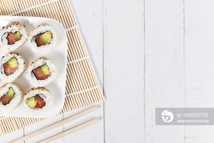Sushi inside out rolls with salmon, avocado and sesame on side of wooden table