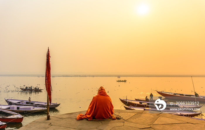 Indian sadhu in traditional saffron attire practicing yoga and meditation in morning at the bank of sacred Ganges river in Varanasi, Uttar Pradesh, India.