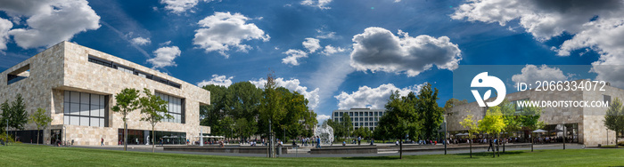 Moderne, quaderförmige Gebäude auf einem Gelände in einer Panoramaaufnahme mit grüner Wiese und aufgelockerter Bewölkung