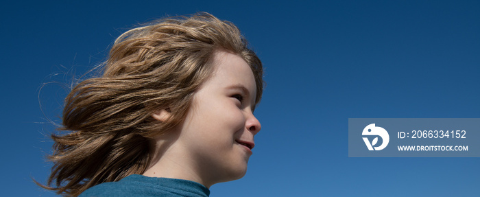 Portrait of a small blond boy looking away on blue sky with copy space, closeup banner. Cute kids face. Positive emotional child.