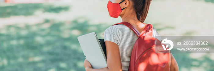 Back to school college student wearing coronavirus mask holding laptop walking in park for remote class online learning education banner.