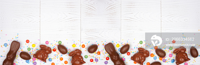 Easter candy, chocolate bunnies and eggs. Overhead view bottom border against a white wood banner background. Copy space.