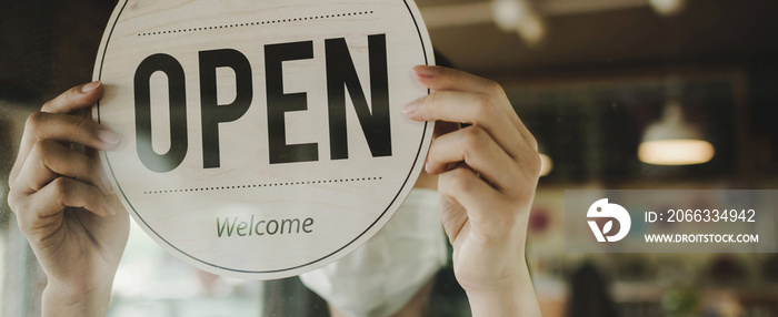 Panoramic banner. waitress wearing protection face mask turning Open sign board reopen after coronavirus quarantine is over in cafe coffee shop ready to service, restaurant, food and drink concept