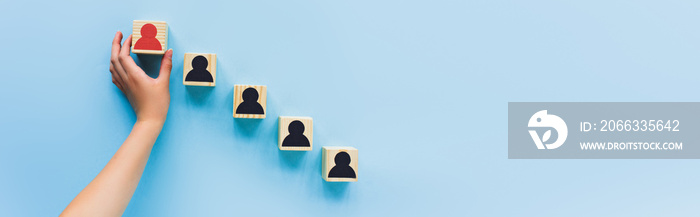 partial view of hand and wooden blocks with black and red human icons on blue background, leadership concept, panoramic shot