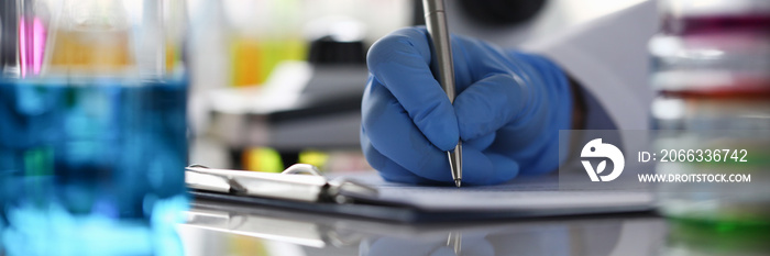 Focus on laboratory worker hand making notes in journal. Person writing down observations and results in report. Lab office investigation and analysis concept