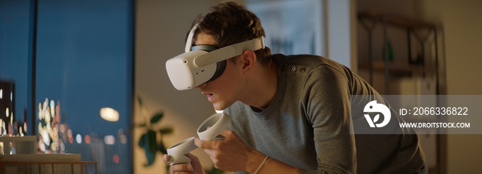 Portait of Caucasian male architect or student using a virtual reality VR headset to work on a house project late at night, preparing for presentation with a client