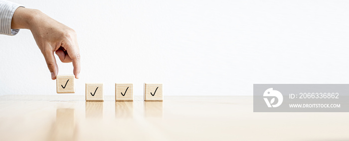 The person is picking up four rectangular wooden blocks with icons placed on them. Concept of Checklist. Banner background with copy space.