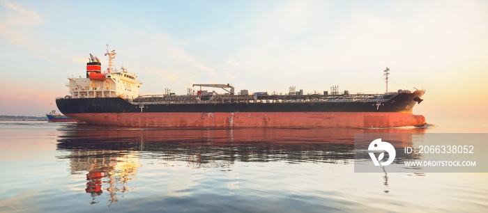 Large cargo ship sailing in the Baltic sea at sunset. Soft golden sunlight. Concept seascape. Panoramic view from the sailing boat. Freight transportation, nautical vessel, logistics