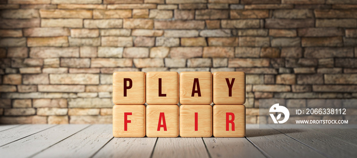 cubes with the message PLAY FAIR in front of a brick wall on wooden floor