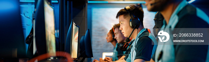 Selective focus on determined Asian cybersport player participating in online video games competition with blurred team members on background