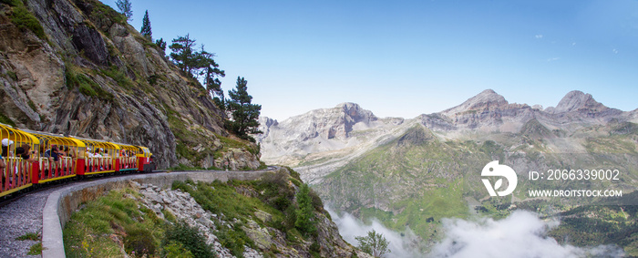 tourist train full of people running through a mountain gorge in the Pyrenees, clouds in the valley below the mountains, Artouste France