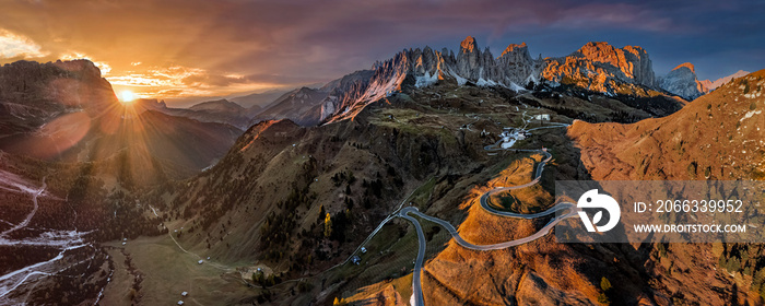 Gardena Pass, Italy - Aerial panoramic view of the curvy roads of the famous Gardena Pass (Passo Gardena) with the peaks of Pizes de Cir, the Italian Dolomites and a warm sunset at autumn season