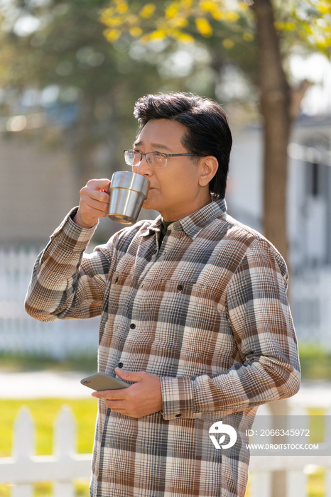 一个老年男人站在露营院子里拿着手机喝咖啡