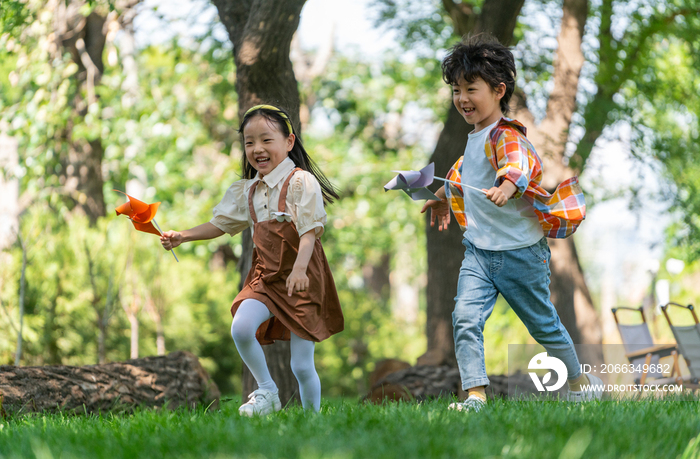 两个小孩子在草地上举着风车开心奔跑