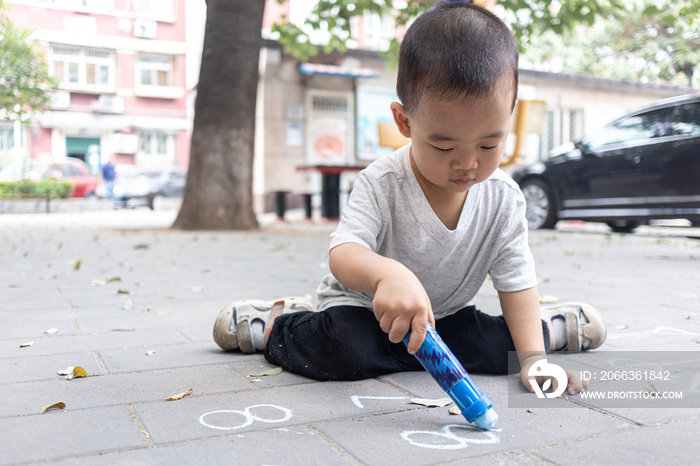 一个小男孩坐在地上用粉笔写字