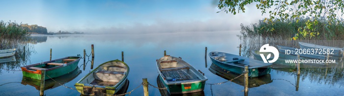 on a lake some rowboats are moored and on the lake there is fog and the lake is quite calm