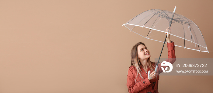 Beautiful young woman holding transparent umbrella on beige background with space for text