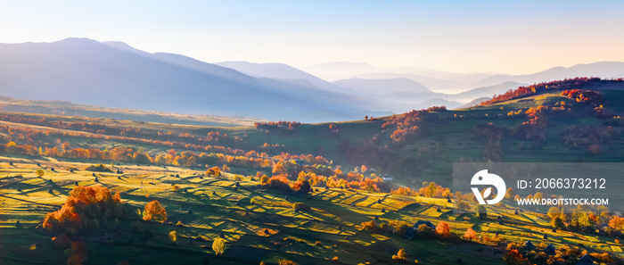 Extraordinary autumn landscape. Green fields with haystacks. Trees covered with orange and crimson leaves. Mountain landscapes.