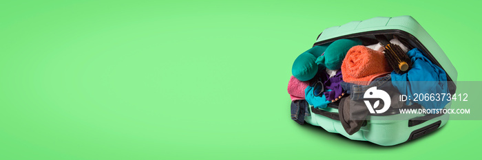 Plastic suitcase with wheels, overflowing things on a green background. Travel concept, vacation trip, visit to relatives. Banner