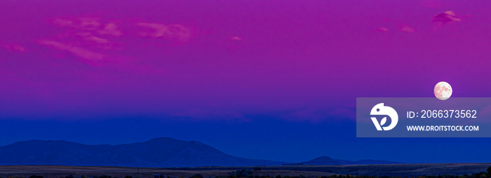 Landscape of an amazing colorful blue and pink and magenta moonscape moon rise during blue hour of a sunset in Montana with a silhouette of the Highwood Mountains