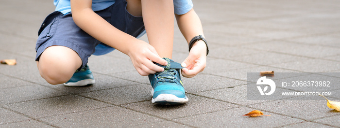 Banner of a young healthy asian schoolboy putting on his running shoes by himself in the playground. Life skills, Self-care, , Comfortable kids shoes, Sport day, Outdoor fun, Get ready concept.