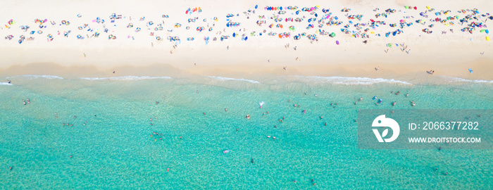 Aerial view crowded public beach with colourful umbrellas, Aerial view of sandy beach with tourists swimming in beautiful clear sea water.