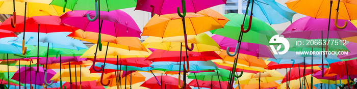 A place in the center of Paris with colorful umbrellas instead of ceiling. Yellow red pink blue green orange. Sunlight coming from the top. Wind is blowing. Banner