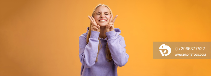 Excited lucky charming friendly blond girlfriend having fun celebrating perfect news best score receive scholarship smiling amused carefree close eyes show peace victory signs, orange background