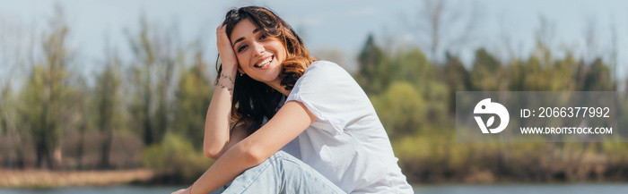 Horizontal image of cheerful woman sitting and looking at camera outside