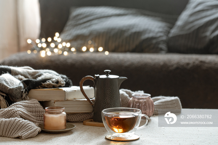Cozy home composition with cup of tea, teapot, candlestick and books on blurred background.