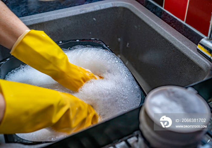 Hands in yellow washing up gloves in a bowl of soapy water