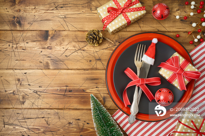 Christmas table setting with black plate, gift box and  decorations on wooden background.
