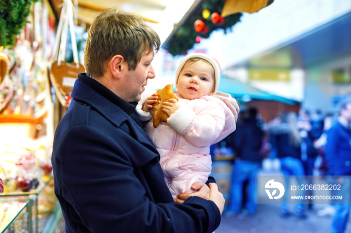 Middle aged father holding baby daughter near sweet stand with gingerbread and nuts. Happy family on