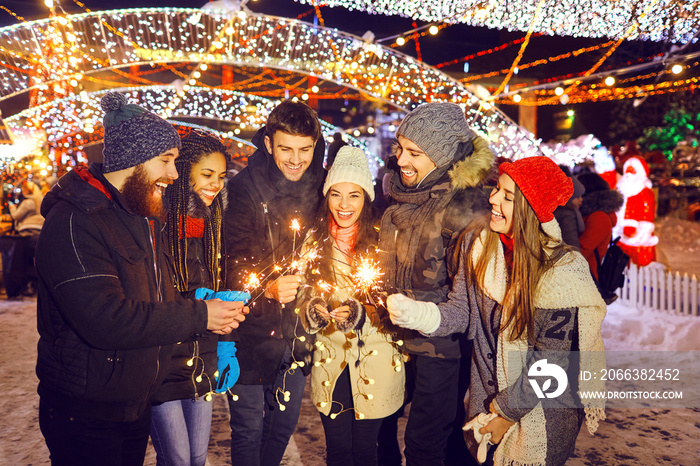 Happy friends with sparklers at a fair at christmas