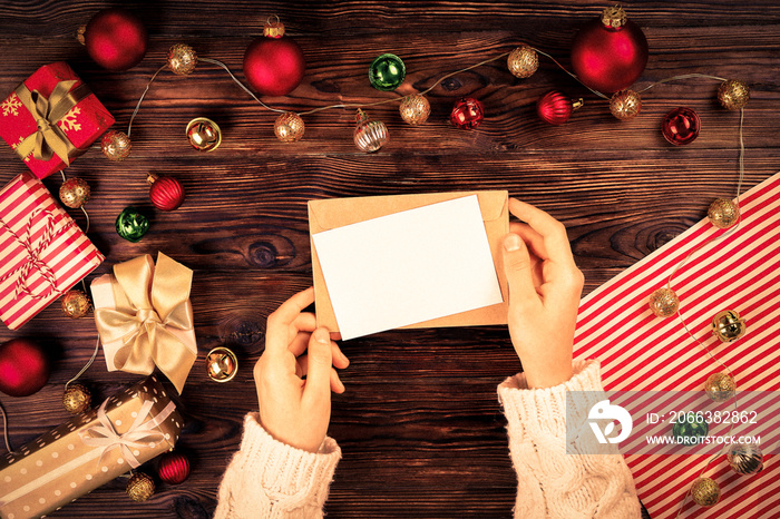 Female hands writing letter to Santa Claus on wooden background with christmas gifts and decoration 